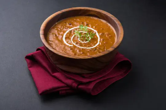 Dal makhani served in a wooden bowl on a dark red cloth