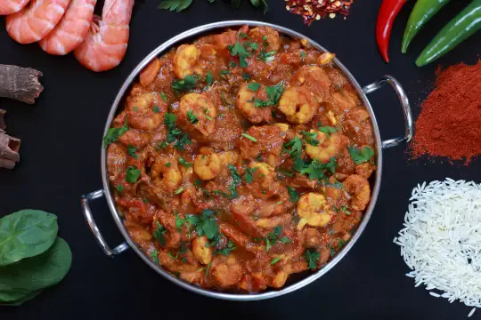 Prawns masala curry served in a steel karahi with rice alongside
